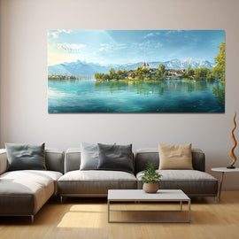 Wide panorama of a calm lake with a chapel-topped promontory and snow-dusted peaks